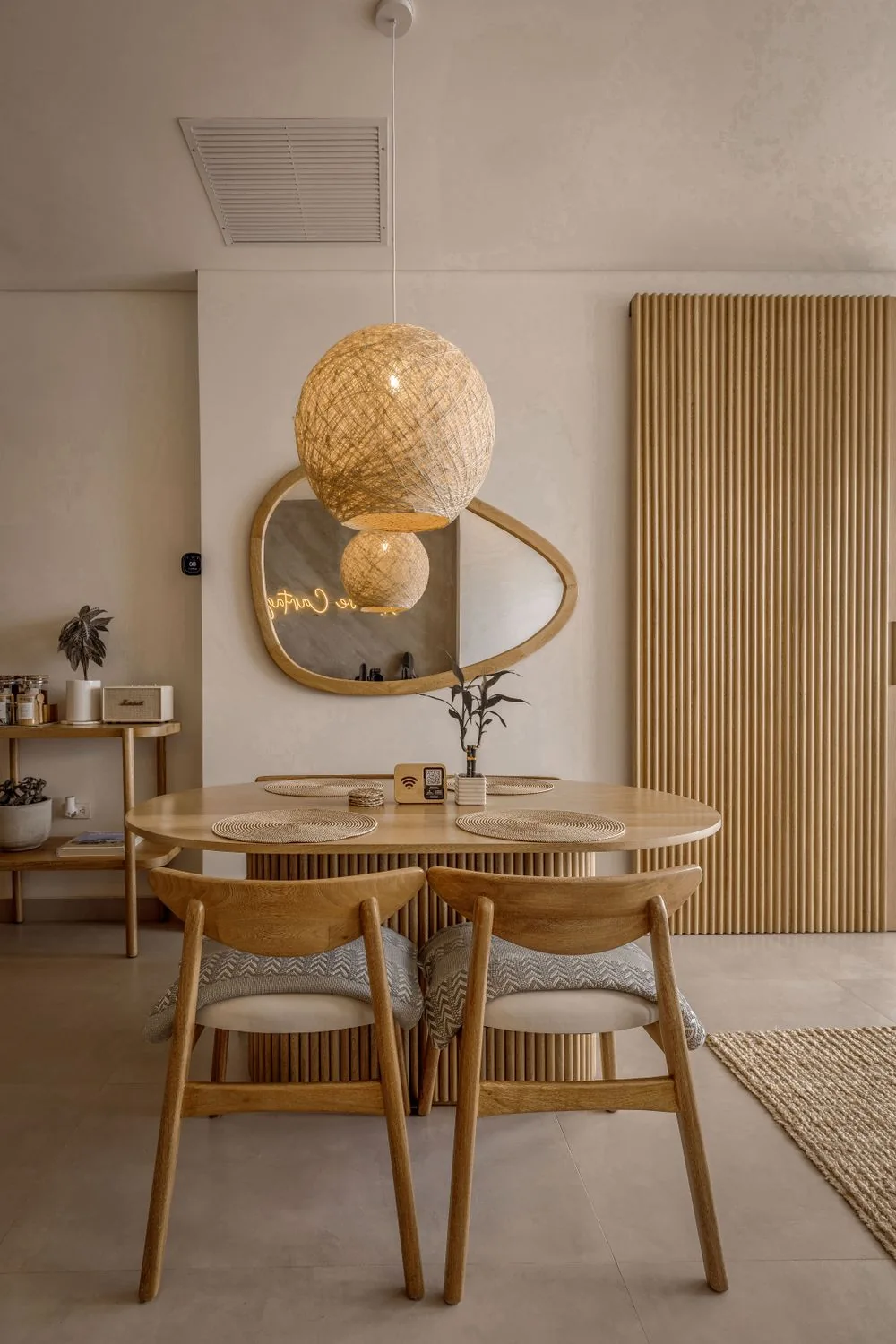 Table et chaises en bois sous une suspension tressée, devant un miroir