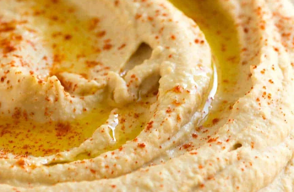 Houmous dans une assiette blanche, avec un filet d’huile d’olive et du paprika
