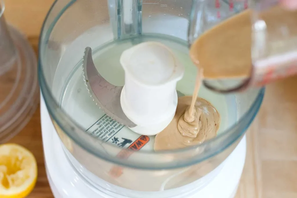Tahin versé dans la cuve d’un robot culinaire, avec un citron pressé à côté