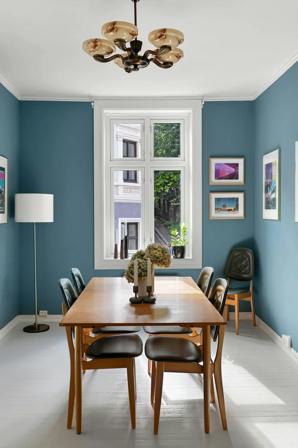 Salle à manger aux murs bleus avec une table en bois, des chaises sombres et une grande fenêtre